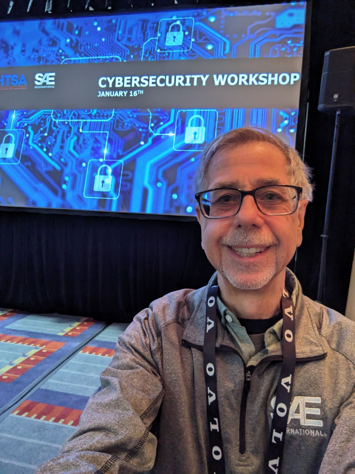 Mark Zachos poses in front of the Cybersecurity workshop graphic at SAE.